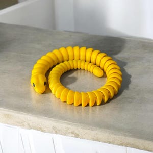 May include: A yellow rubber snake toy coiled into a circle. The snake has black eyes and a textured surface.