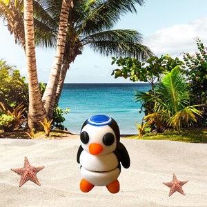 May include: A white and black penguin figurine with a blue hat, standing on a sandy beach with two starfish. The penguin has black eyes, an orange beak, and white and black wings.