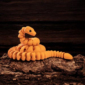 Op de afbeelding: Een opgerolde oranje slangfiguur met een getextureerd oppervlak. De slang is in een opgerolde positie geplaatst met zijn kop omhoog.