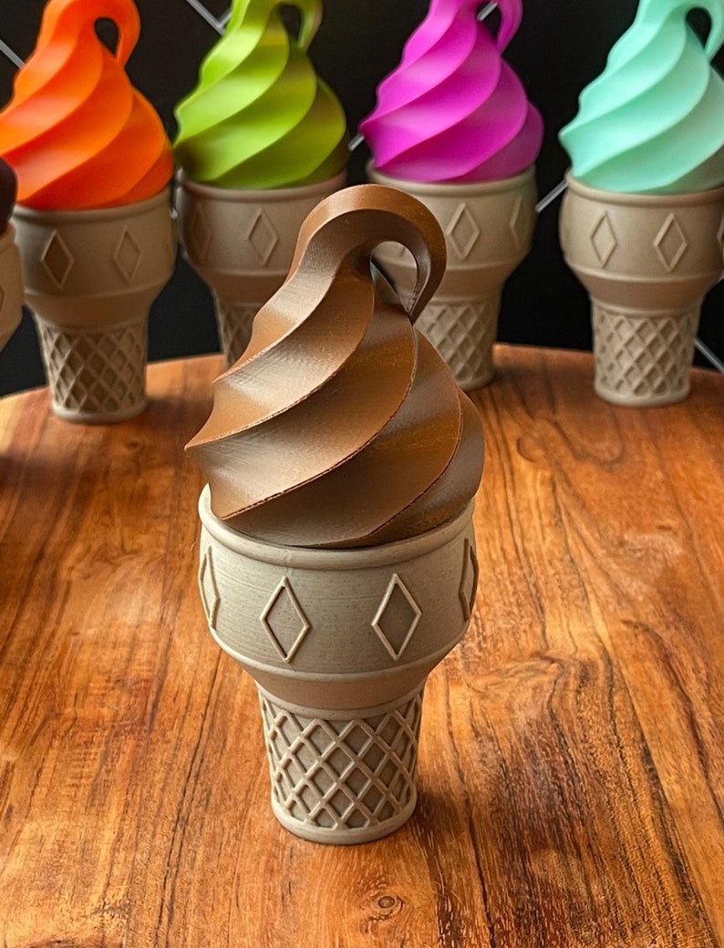 May include: A chocolate ice cream cone with a swirl of chocolate ice cream on top. The cone is sitting on a wooden surface.