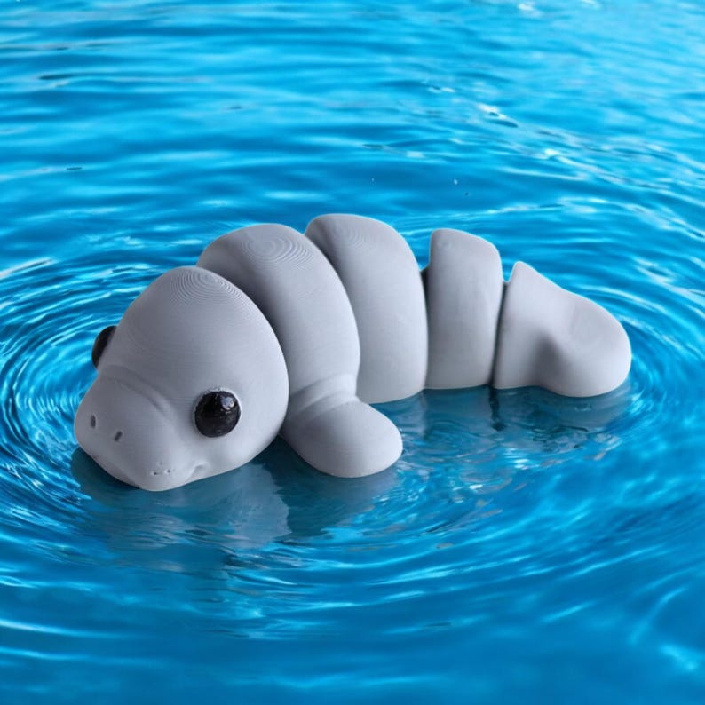 May include: A gray, segmented, toy manatee floats in a blue pool of water. The manatee has black eyes and a small, upturned snout.
