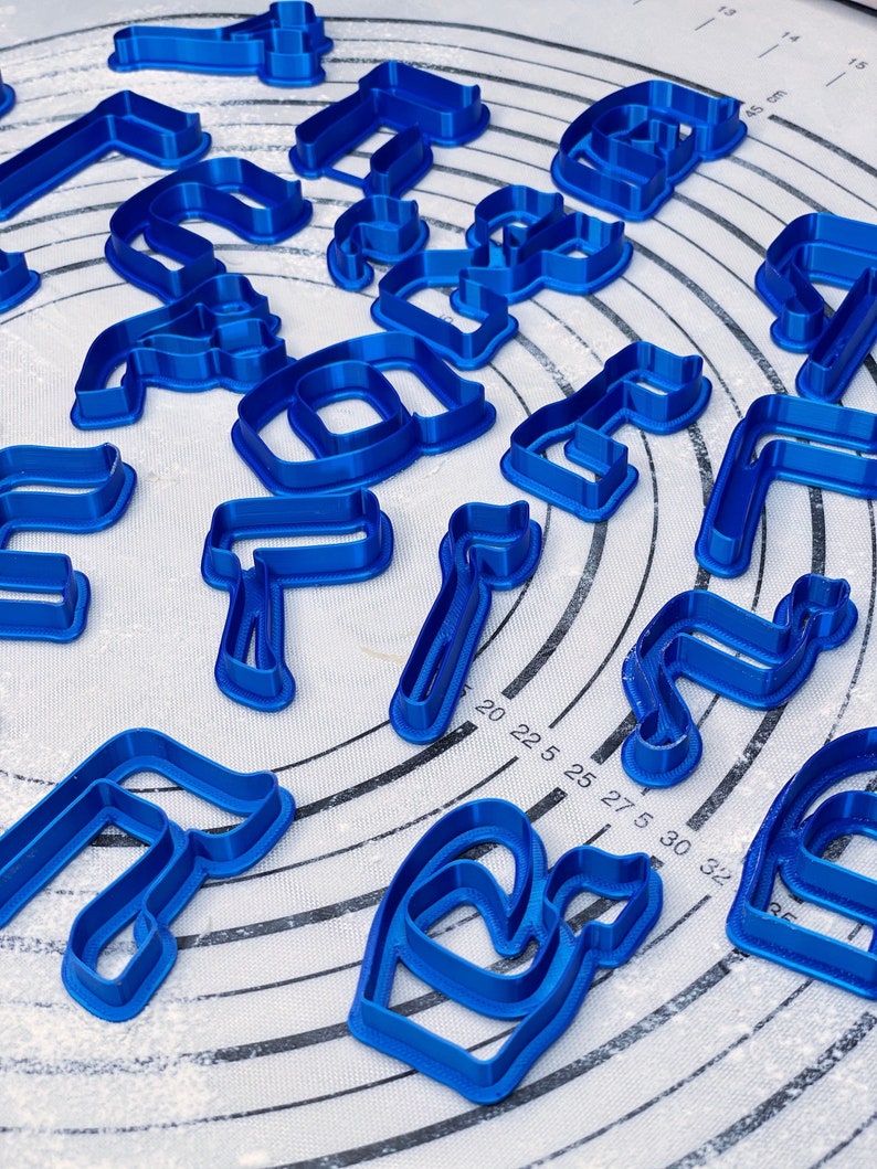 May include: A set of blue plastic cookie cutters in various shapes, including letters and abstract designs. The cutters are arranged on a white surface with a circular pattern.