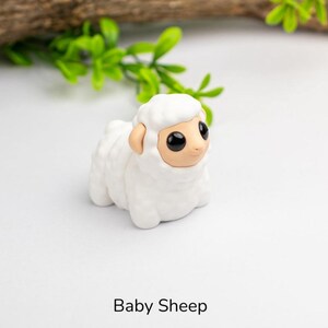 Puede incluir: Peque&ntilde;a figura de cordero blanco con textura de lana esponjosa. La oveja tiene cara y orejas color beige, y ojos grandes y negros. El texto "Baby Sheep" est&aacute; impreso en negro en la parte inferior de la imagen.