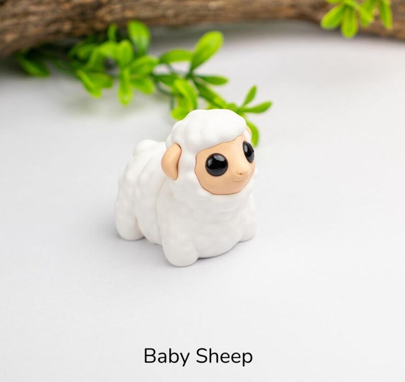 Puede incluir: Peque&ntilde;a figura de cordero blanco con textura de lana esponjosa. La oveja tiene cara y orejas color beige, y ojos grandes y negros. El texto "Baby Sheep" est&aacute; impreso en negro en la parte inferior de la imagen.