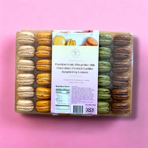 May include: A clear plastic container filled with 36 assorted macarons. The macarons are arranged in rows of six, with each row containing a different flavor. The flavors are: Passion Fruit, Pistachio, Milk Chocolate, French Vanilla, Raspberry, and Lemon. The container is labeled with the flavors and a nutrition facts label. The label also states that the macarons are gluten free.