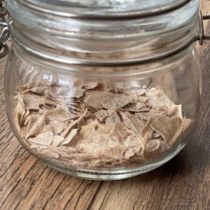 Puede incluir: Un tarro de vidrio con tapa de metal lleno de copos de cereal marrones de forma irregular.