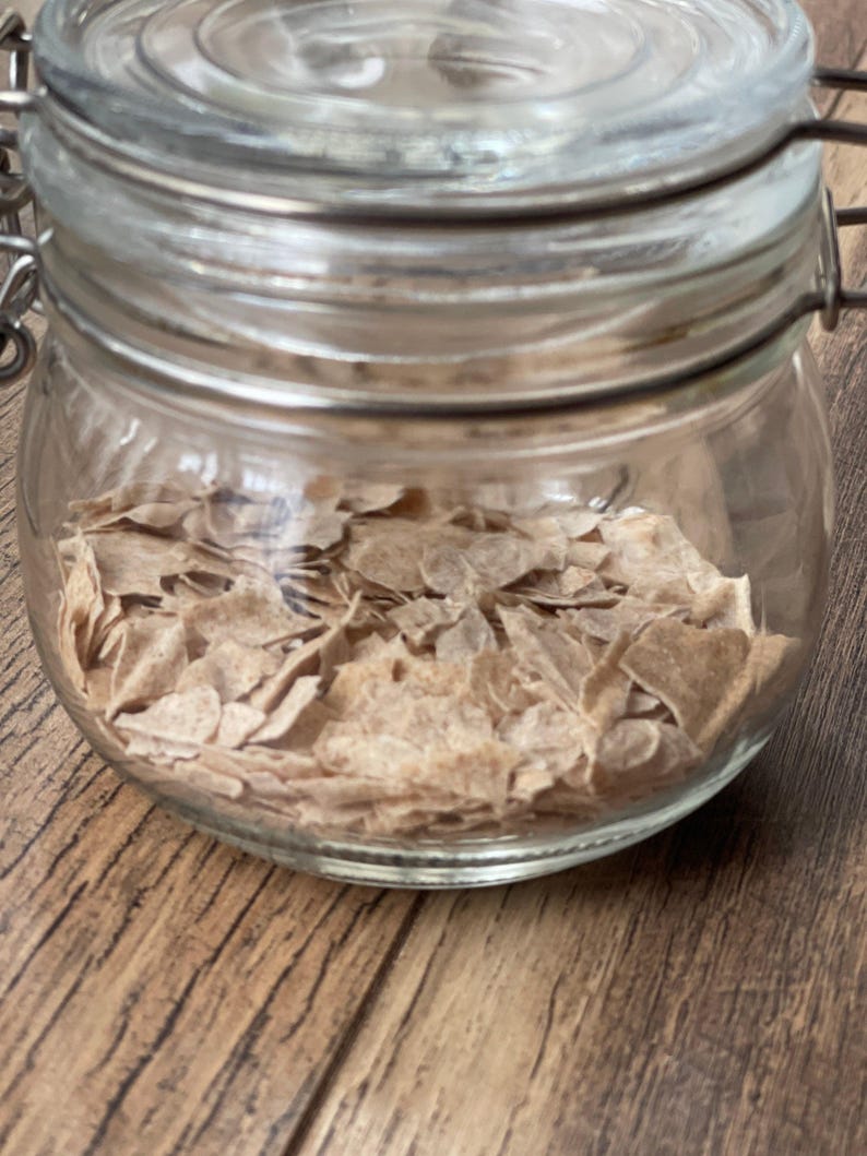 Puede incluir: Un tarro de vidrio con tapa de metal lleno de copos de cereal marrones de forma irregular.