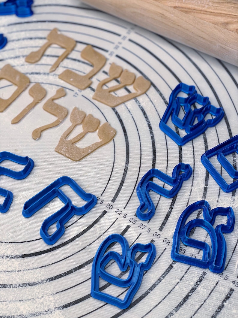 May include: Blue and brown plastic cookie cutters in the shape of Hebrew letters and menorahs on a white surface with flour.