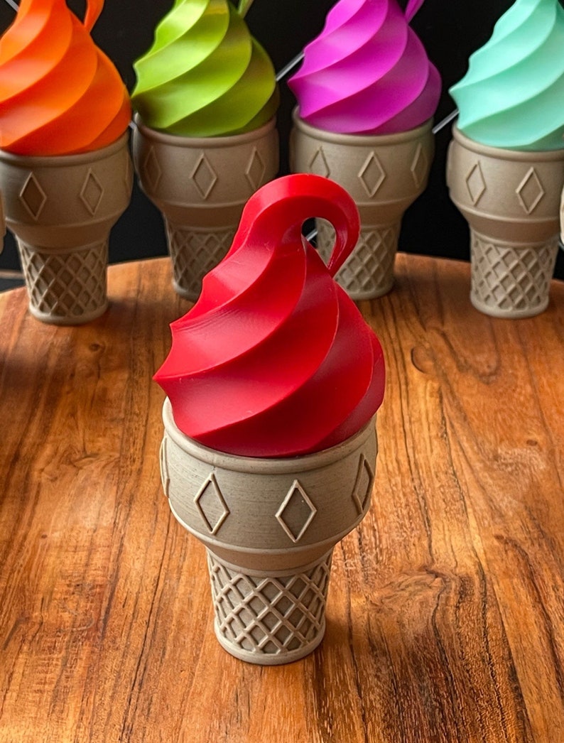 May include: A red ice cream cone with a swirl of ice cream on top. The cone is made of a light brown material and has a waffle pattern.