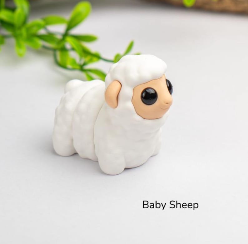 Puede incluir: Figura de oveja blanca hecha a mano con cuerpo esponjoso y cara, orejas y ojos negros grandes de color beige. El texto "Baby Sheep" est&aacute; impreso debajo.