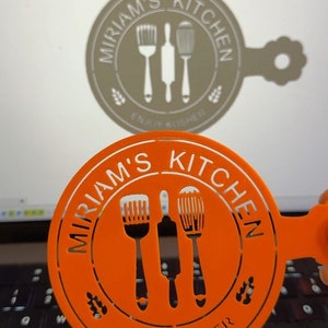 May include: Orange plastic stencil with the text "Miriam's Kitchen" and "Enjoy Kosher" in white. The stencil features three kitchen utensils: a whisk, a rolling pin, and a spatula.
