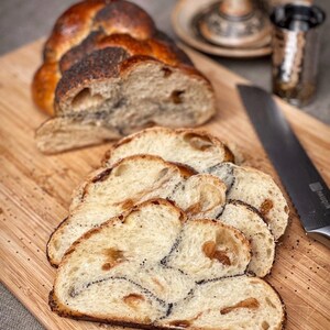 May include: A loaf of braided bread with poppy seeds, sliced on a wooden cutting board. The bread is light brown and has a golden crust.