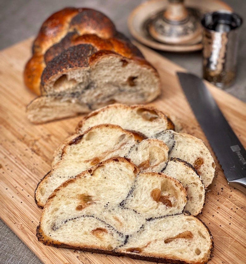 May include: A loaf of braided bread with poppy seeds, sliced on a wooden cutting board. The bread is light brown and has a golden crust.