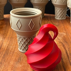 May include: A red swirl ice cream cone shaped container with a beige ice cream cone shaped container next to it. The containers are on a wooden surface.