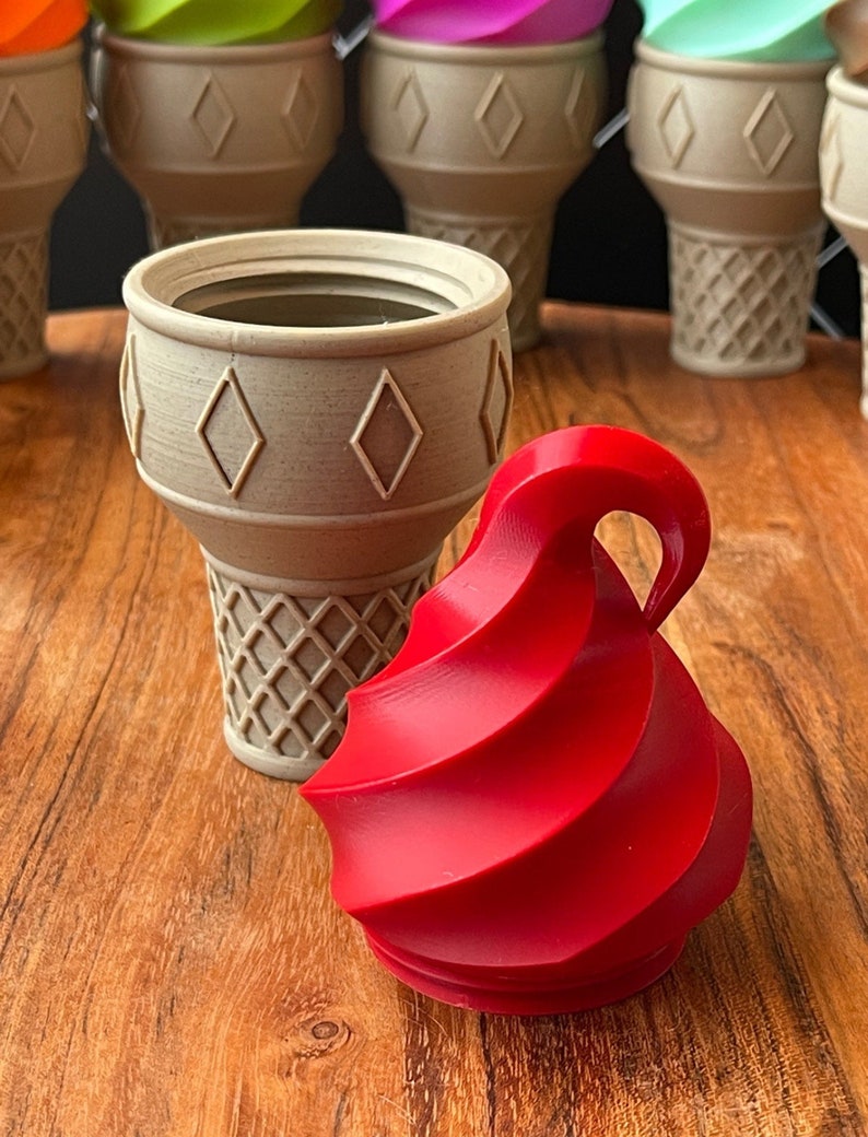 May include: A red swirl ice cream cone shaped container with a beige ice cream cone shaped container next to it. The containers are on a wooden surface.