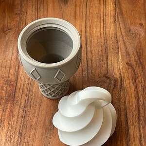 Op de afbeelding: Een witte keramische ijshoornvormige container met een afneembaar deksel. Het deksel is gevormd als een swirl van ijs.