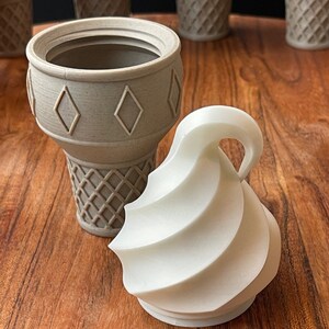 Op de afbeelding: Een set van vier grijze ijshoornvormige containers met een wit swirl ijsdeksel. De containers hebben een diamantpatroon aan de bovenkant en een wafelpatroon aan de onderkant.