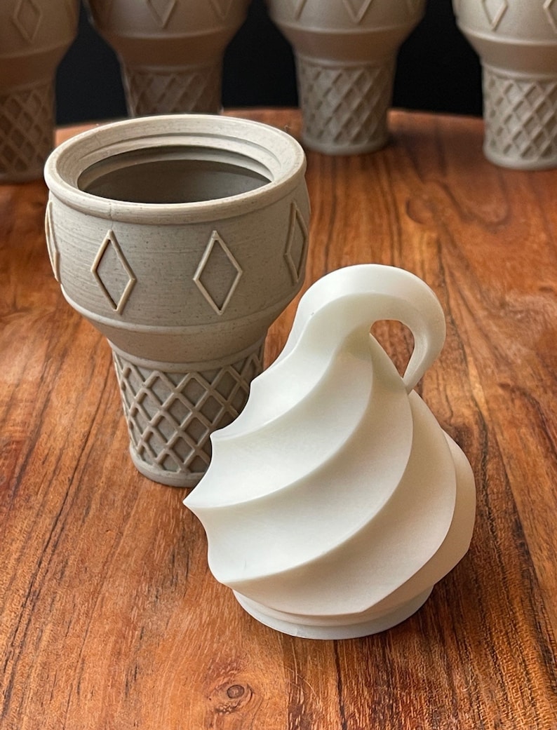 Op de afbeelding: Een set van vier grijze ijshoornvormige containers met een wit swirl ijsdeksel. De containers hebben een diamantpatroon aan de bovenkant en een wafelpatroon aan de onderkant.