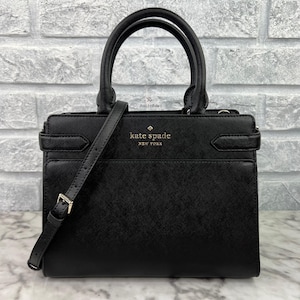 May include: Black leather Kate Spade satchel handbag with a gold logo and a detachable shoulder strap.