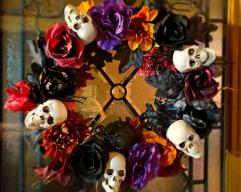 May include: A Halloween wreath with black, red, and purple flowers, and white skull ornaments. The wreath is decorated with black and gold glitter and has a black spider in the center. The wreath is on a wooden door with a glass panel.