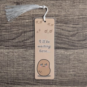 May include: A brown bookmark with a cartoon potato with a face and the text "I'll be waiting here..." printed on it. The bookmark has a white tassel.