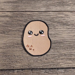 May include: A brown embroidered patch of a cartoon potato with a smiling face and black eyes. The potato has a few brown spots on it.