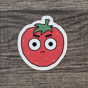 May include: A red strawberry with a white outline and a green stem. The strawberry has a cartoon face with angry eyebrows, big eyes, and a frowning mouth.