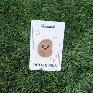 May include: A brown potato pin with a cute cartoon face and the text "I'm a potato!" on a white card with the text "Homemade Potato Pins IG @potatomoji".