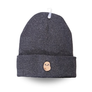 Puede incluir: Un gorro gris con una patata marrón con una cara sonriente bordada en la parte delantera.