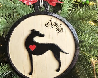 May include: A round wooden ornament with a black border and a black silhouette of a dog with a red heart on its chest. The ornament is personalized with the name "Arlo" in black cursive lettering.