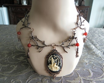 May include: A copper branch necklace with a cameo pendant featuring a woman in a forest setting. The necklace is adorned with red carnelian beads and dangling charms.
