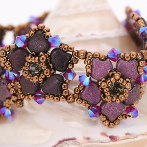 May include: A purple and copper beaded bracelet with iridescent crystals. The bracelet features a floral design with multiple flower shapes.