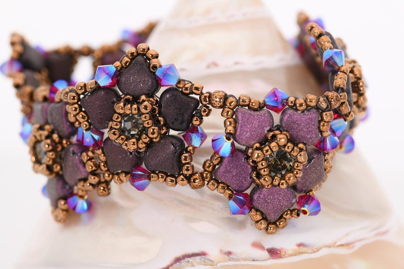 May include: A purple and copper beaded bracelet with iridescent crystals. The bracelet features a floral design with multiple flower shapes.