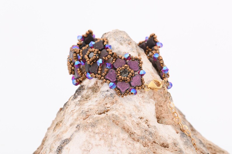 May include: A beaded bracelet with a floral design. The bracelet is made with brown, purple, and blue beads. The bracelet is on a rock.