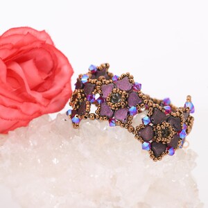 May include: A purple and brown beaded bracelet with a flower design. The bracelet is made with small, iridescent beads and is accented with clear crystals.