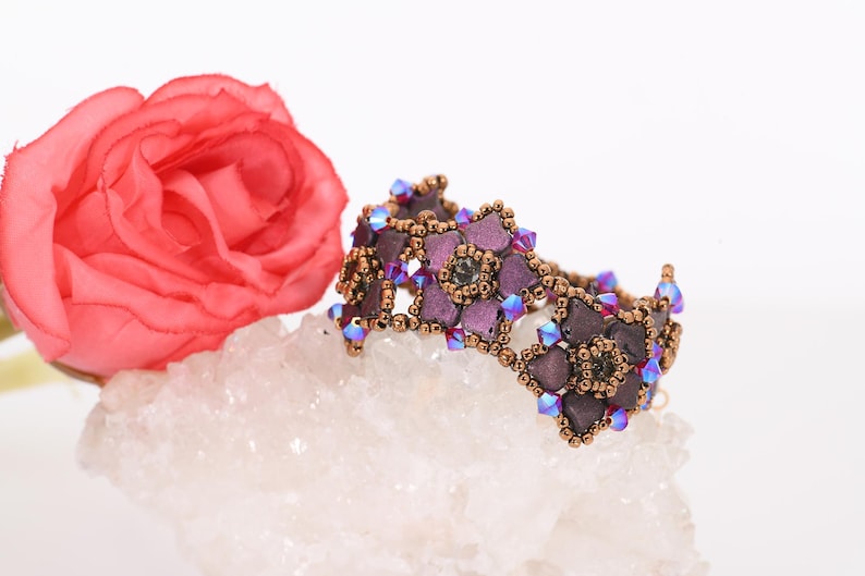 May include: A purple and brown beaded bracelet with a flower design. The bracelet is made with small, iridescent beads and is accented with clear crystals.