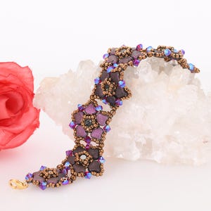 May include: A purple and brown beaded bracelet with a flower design. The bracelet is on a white background with a pink rose.