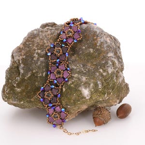 May include: A purple and brown beaded necklace with a floral design. The necklace is on a rock with acorns.