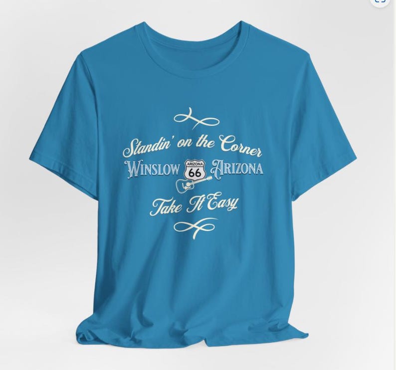 May include: A turquoise blue t-shirt with a white graphic design that says "Standin' on the Corner Winslow Arizona" with a Route 66 sign and a guitar. The text "Take It Easy" is below the graphic.