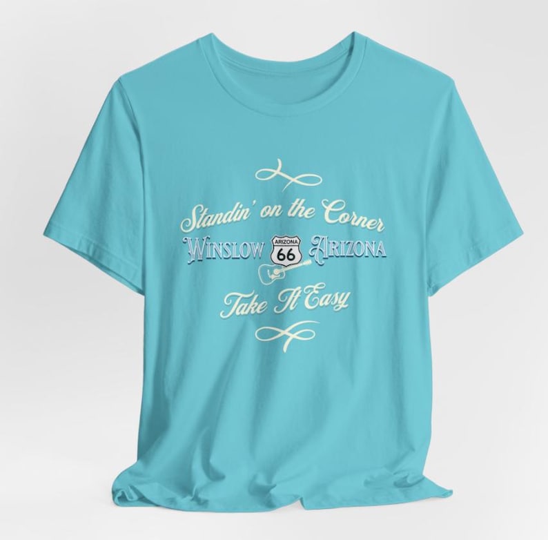 May include: A turquoise blue t-shirt with a white graphic print that says "Standin' on the Corner Winslow Arizona" with a Route 66 sign and a guitar. The text "Take It Easy" is printed below the graphic.