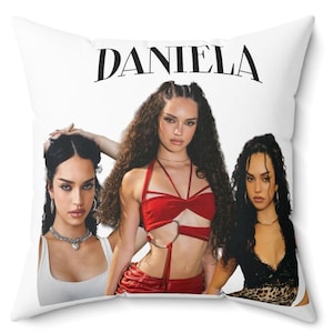 Può includere: Cuscino quadrato bianco con tre donne con lunghi capelli ricci scuri. La parola "DANIELA" è stampata in nero in alto. Le donne indossano vari outfit, tra cui un top e una gonna rossi e un top nero.