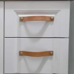 Può includere: Due cassetti bianchi per armadietto dotati di maniglie in pelle color marrone chiaro. Ogni maniglia è fissata al frontale del cassetto con due borchie metalliche circolari color argento. I frontali presentano un design a pannello incassato.