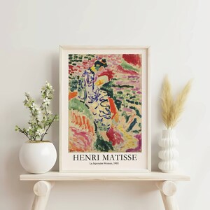 K&ouml;nnte beinhalten: Ein farbenfrohes abstraktes Gem&auml;lde von Henri Matisse mit dem Titel "La Japonaise Woman, 1905". Das Gem&auml;lde zeigt eine Frau in einem blau-wei&szlig;en Kleid, die in einer Landschaft aus Gr&uuml;n, Rot und Gelb steht.