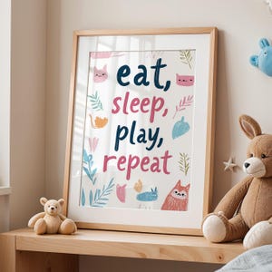 Könnte beinhalten: Ein gerahmter Druck mit weißem Hintergrund und bunten Illustrationen von Katzen, Blättern und einem Fuchs. Der Text auf dem Druck lautet "eat, sleep, play, repeat".