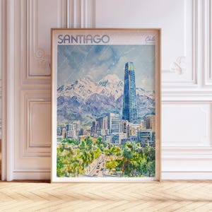 Puede incluir: Impresión en acuarela de Santiago, Chile, con el horizonte de la ciudad con un rascacielos alto y montañas nevadas al fondo. La impresión está enmarcada en un marco de madera marrón claro. La palabra "Santiago" está en la parte superior.