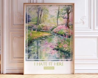 May include: A framed print of a watercolor painting depicting a lush green forest with a stream running through it. The stream is surrounded by pink flowers and the text "I HATE IT HERE" is printed below the image.