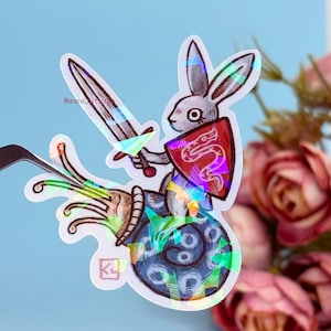 Könnte beinhalten: Ein holografischer Aufkleber mit einem weißen Kaninchen, das ein Schwert und einen roten Schild mit einem Schlangenmuster hält. Das Kaninchen reitet auf einer blauen und weißen Schnecke mit einem grünen Stiel.
