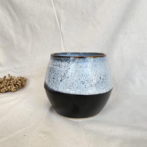 Op de afbeelding: Een set van drie keramische mokken met een gespikkelde, matte afwerking. De mokken zijn in crème, lichtgrijs en donkergrijs. Elke mok heeft een eenvoudig, minimalistisch ontwerp.