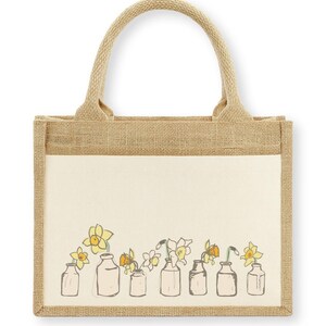 May include: A rectangular jute tote bag with a cream-colored front panel. The panel features a line of sketched yellow daffodils in various glass jars. The bag has a natural jute handle and trim, perfect for carrying groceries or other items.