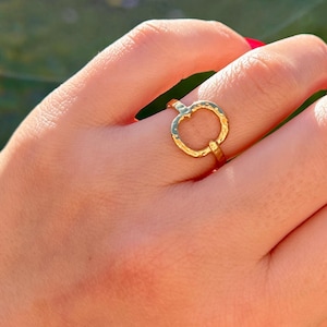 Peut inclure: Une bague dorée avec un motif de cercle ouvert. La bague est portée au doigt et le motif présente une surface texturée. La bague est un bijou.